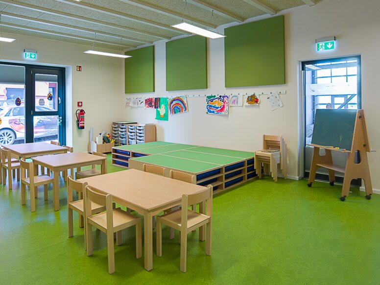 Gruppenraum der Kindertagesstätte „In der Kammgarnspinnerei“ Gruppenraum einer Kindertagesstätte mit grünem Boden und Tischen und Stühlen aus Holz